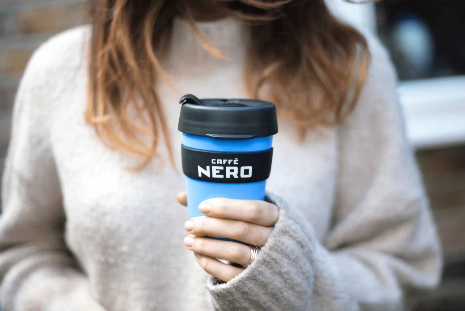 A woman holding a Caffè Nero branded reusable coffee cup